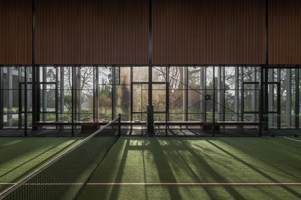 filtered-morning-light-through-trees-and-architectural-timber-fins-into-interior-of-padel-club-court-at-sunrise-adare-manor