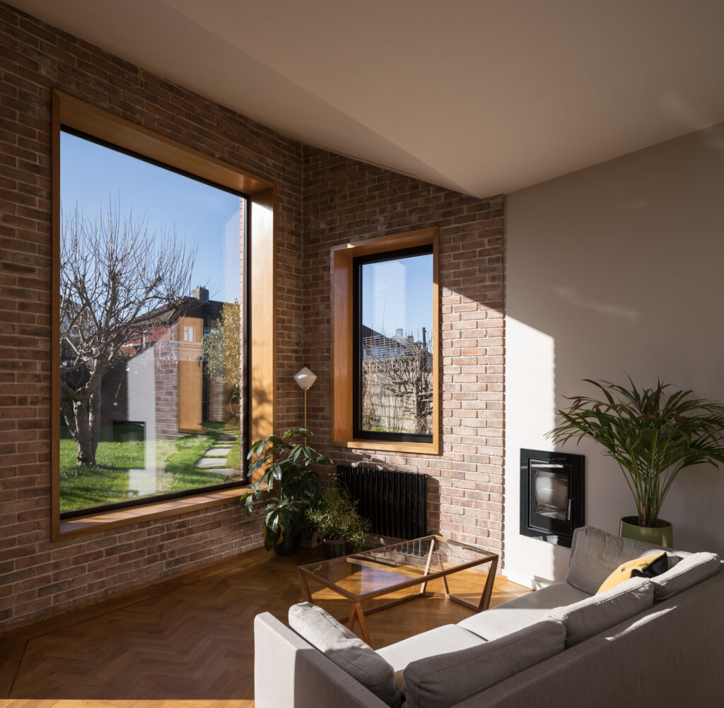 living-area-with-angled-roof-and-brick-and-white-plastered-wall-with-view-to-garden-through-timber-framed-windows