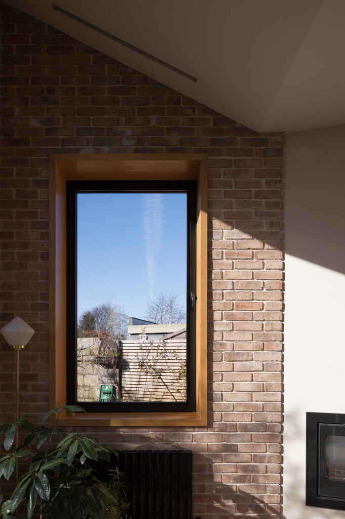 angled-roof-and-brick-and-white-plastered-wall-with-view-to-garden-through-timber-framed-window