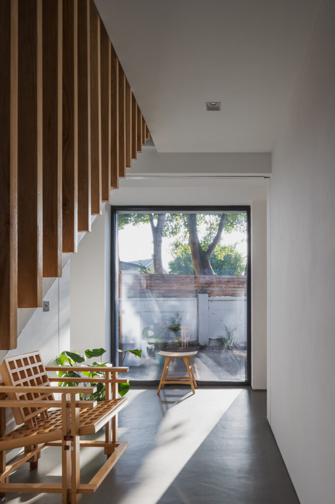 light-shaft-streaming-onto-concrete-floor-and-wooden-chairs-of-hallway-with-wooden-balustrade-stairs