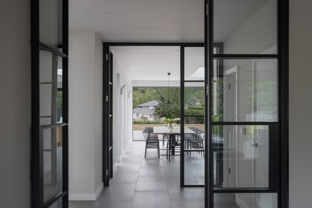 long-wooden-table-and-dining-chairs-in-white-walled-and-grey-tiled-dining-area-viewed-through-crittal-doors