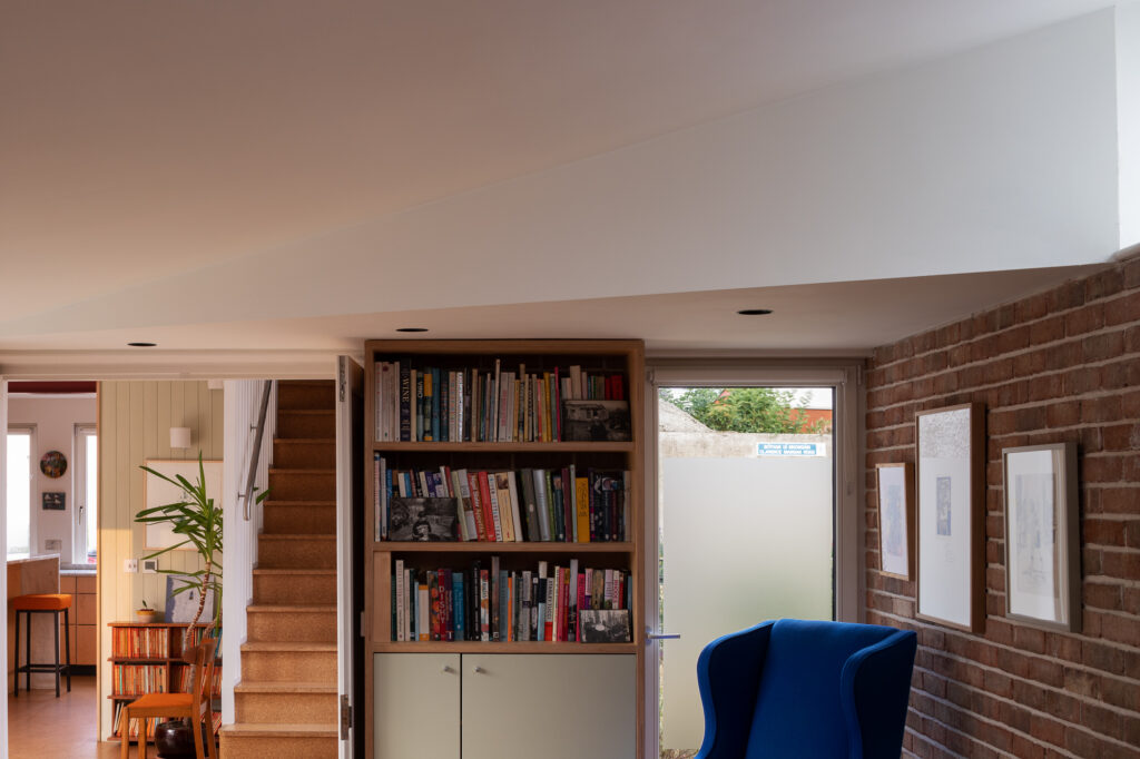 angled-roof-over-reading-area-with-bookshelves-and-blue-armchair-with-view-to-kitchen