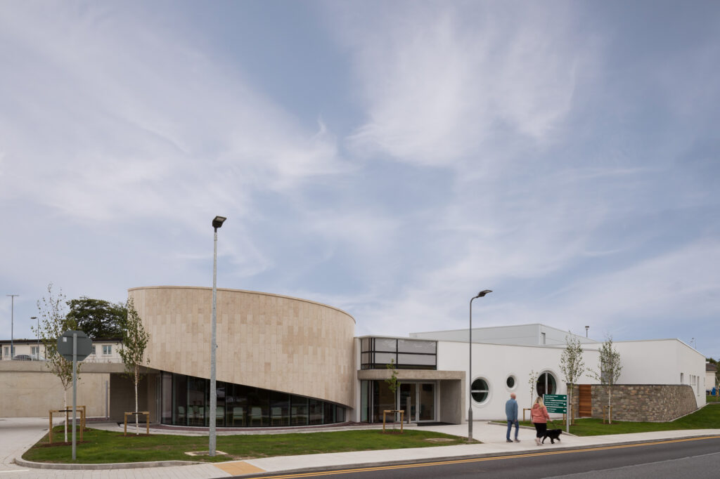 exterior-view-of-university-hospital-waterford-new-mortuary-entrance-with-contemporary-curved-prayer-room-clad-in-stone-as-a-man-woman-and-dog-walk-past