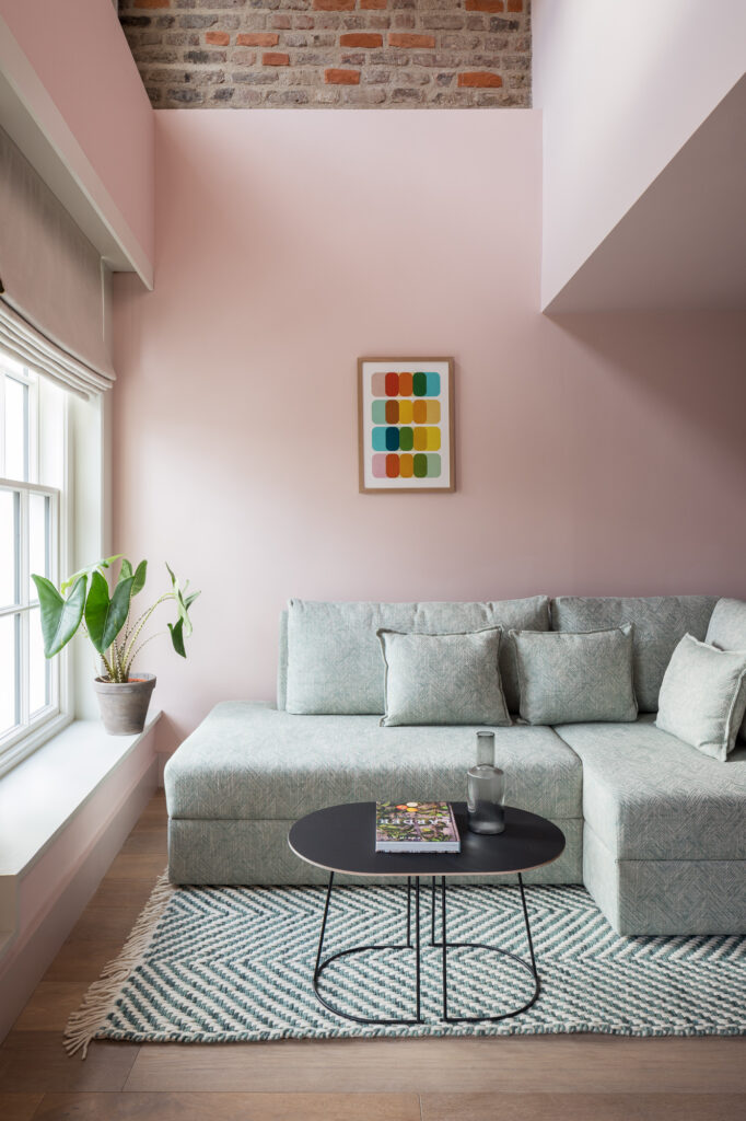 green-l-shaped-couch-at-window-with-pink-rendered-wall-and-brick