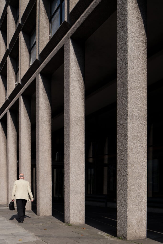 sunlight-casting-shadows-on-agriculture-house-arcade-with-exposed-aggregate-concrete-columns-as-man-in-jacket-walks-by