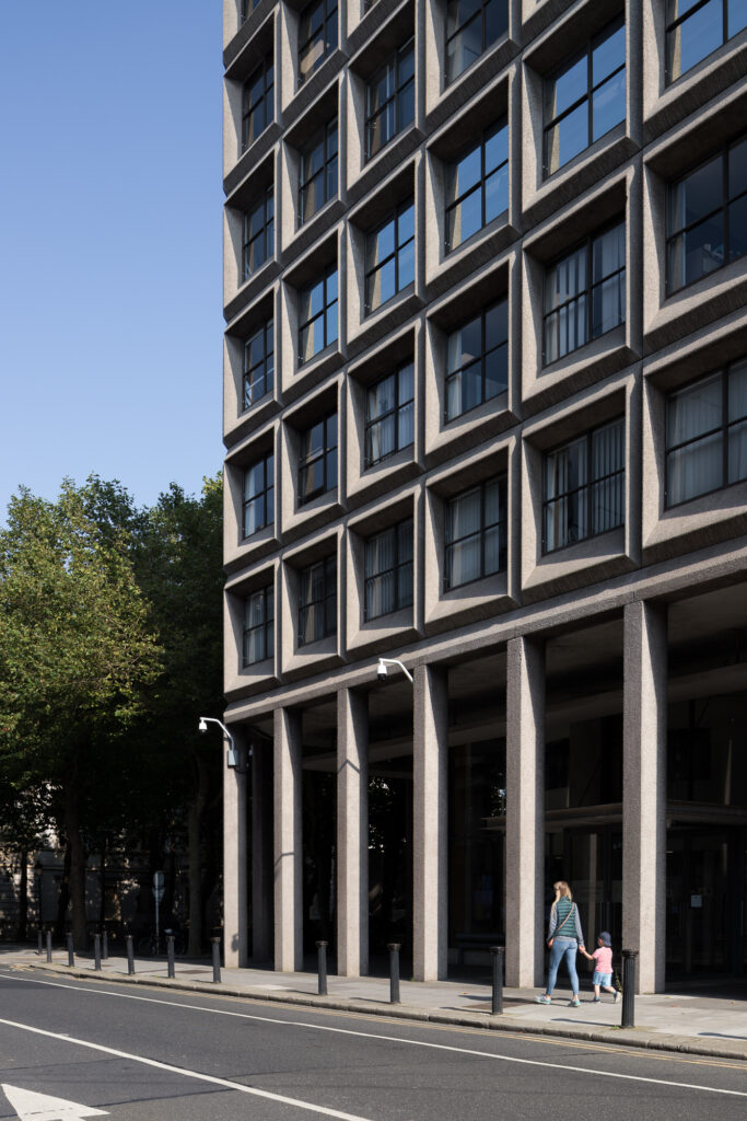 sunlight-casting-shadows-on-sam-stephenson's-agriculture-house-arcade-with-exposed-aggregate-concrete-columns-as-mother-and-son-walk-by