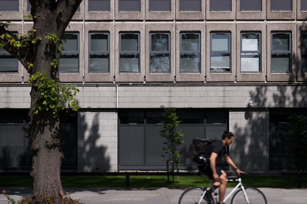 man-cycling-by-pre-cast-concrete-building-with-grey-tiled-elevation-at-ground-floor