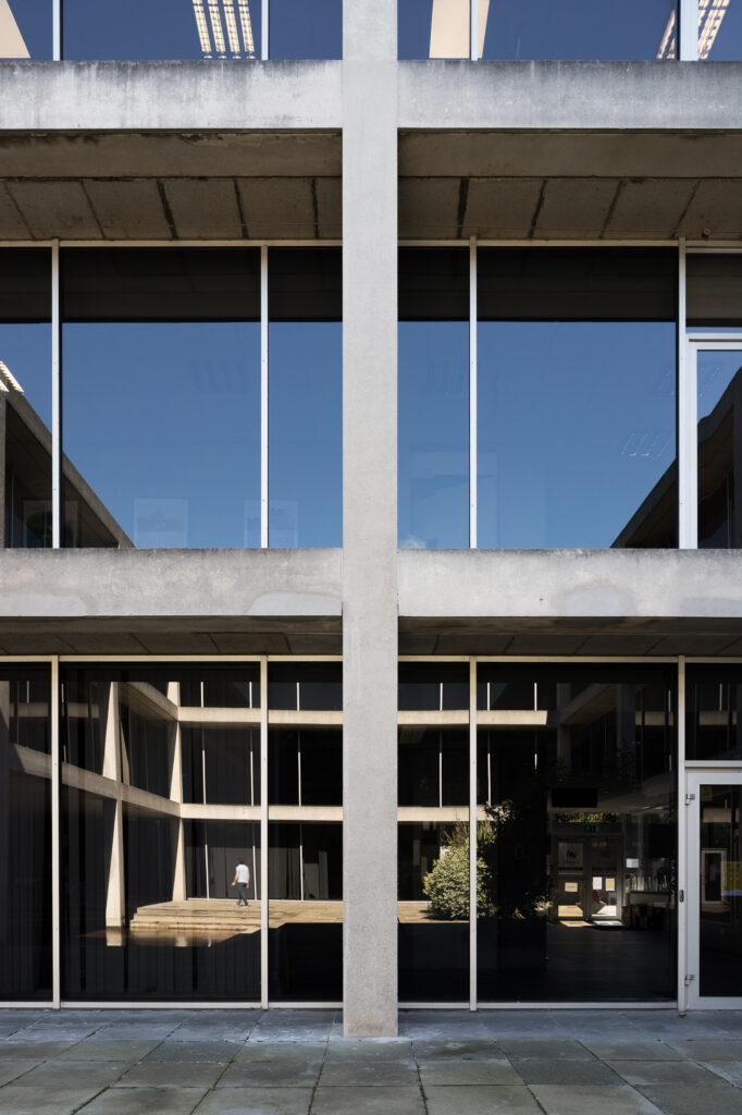 exposed-concrete-and-reflective-glass-structure-reflects-courtyard-as-man-in-t-shirt-walks-through