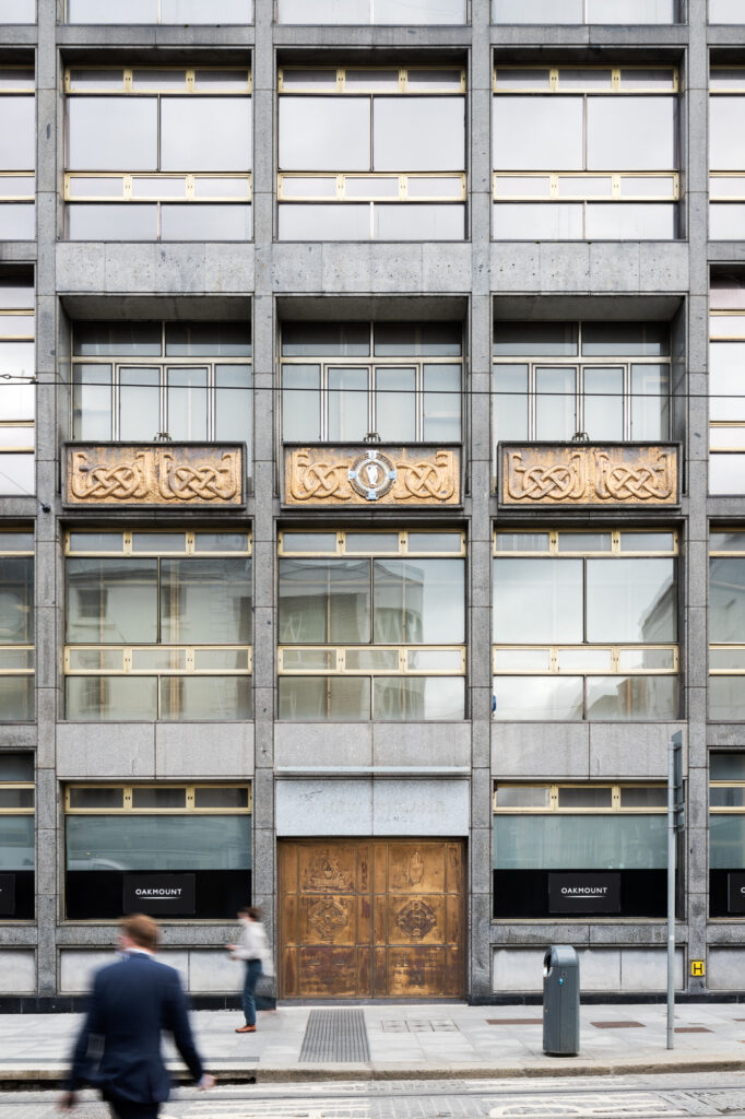 elevation-of-new-ireland-assurance-building-with-limestone-panels-and-golden-framed-windows-as-people-walk-by