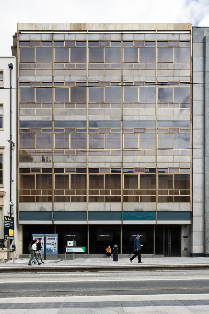 elevation-of-five-storey-new-ireland-assurance-building-with-limestone-panels-and-golden-framed-windows-as-people-walk-by