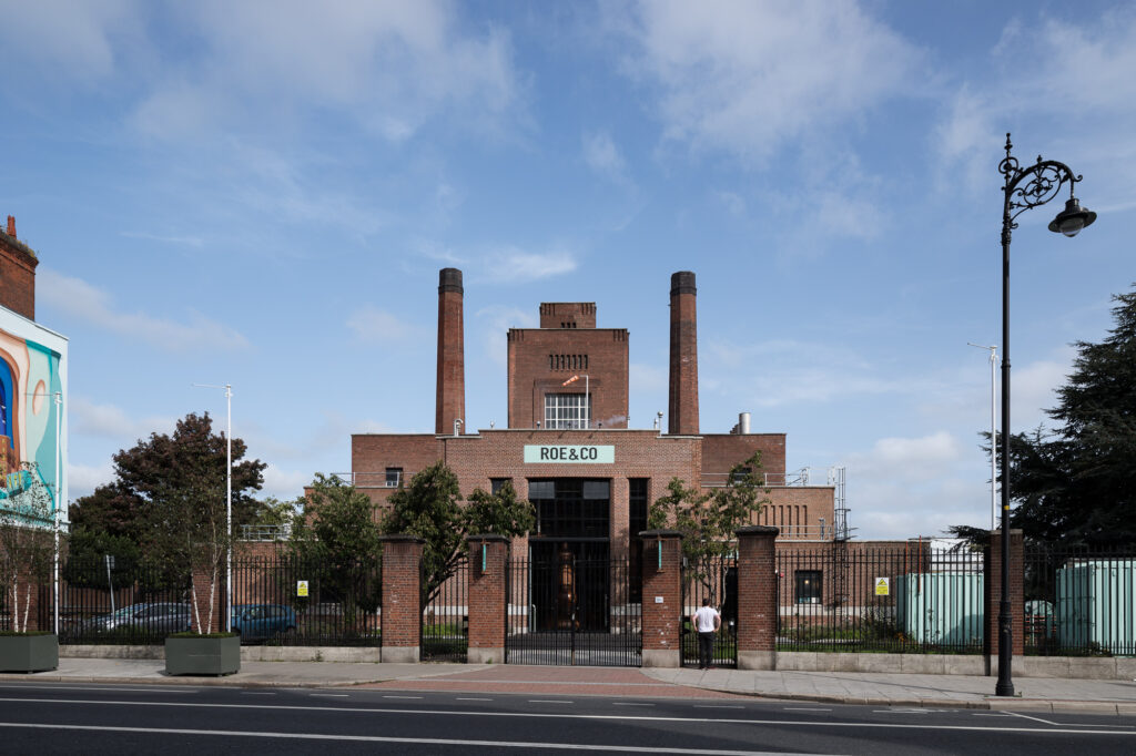 front-elevation-of-red-brick-former-power-plant-roe-&-co-distillery-from-street-with-man-in-white-t-shirt-standing-at-railing