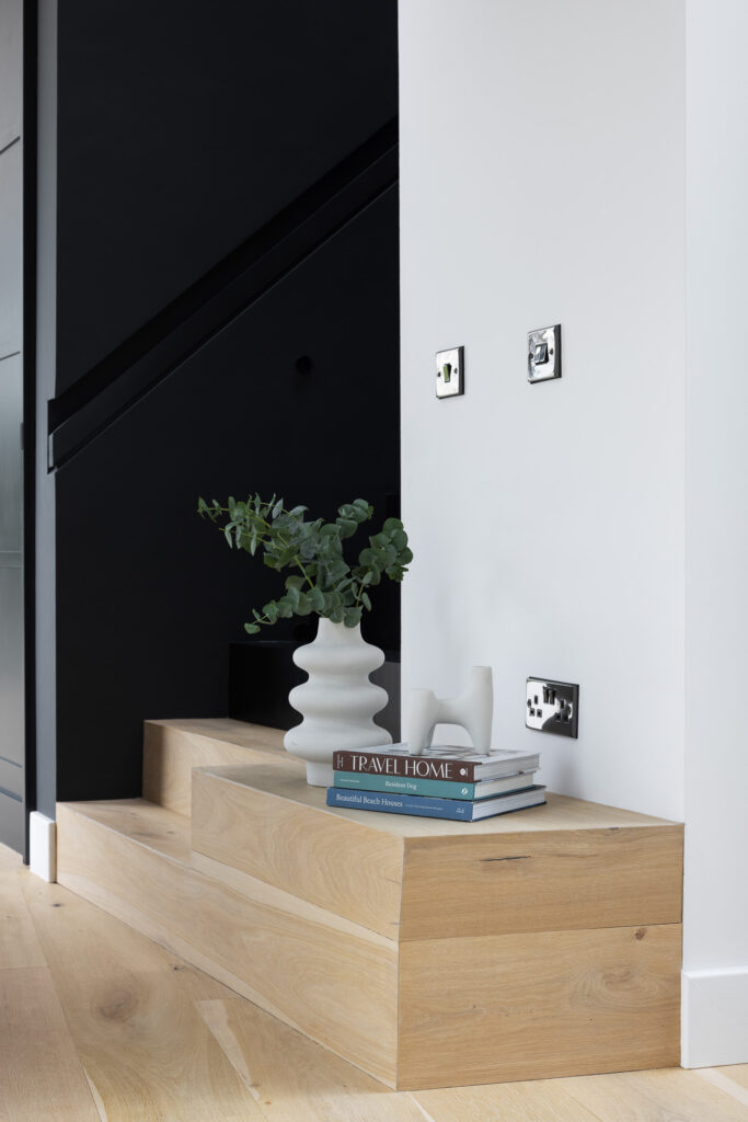 wooden-steps-with-books-and-white-sculpture-on-top-and sculptured-vase with-plant-beside-black-stairway
