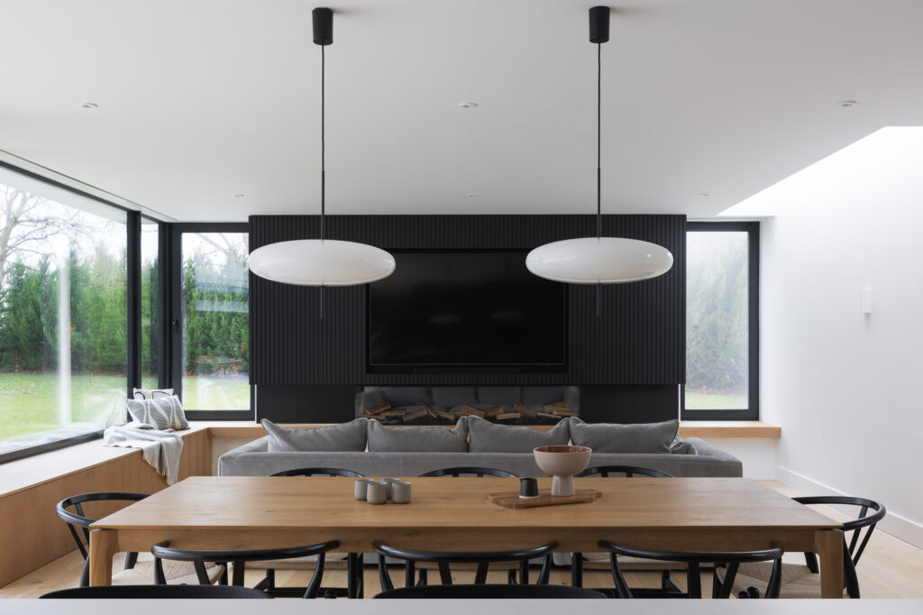 wooden-dining-table-with-pastel-coloured-cups-and-vase-in-foreground-with-living-area-with-couch-and-built-tv-and-fireplace-in-background