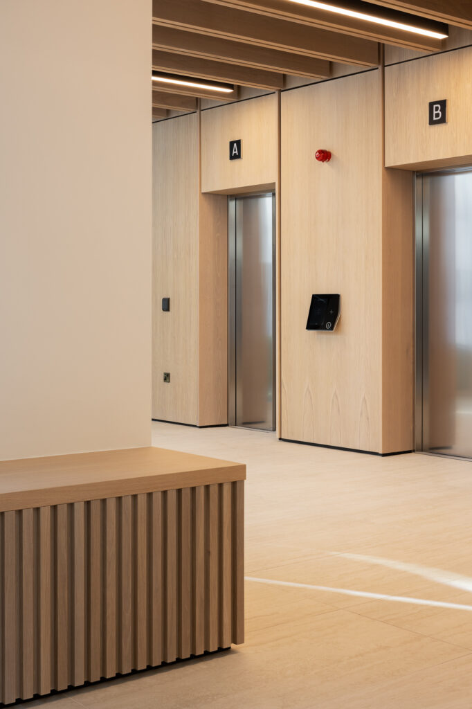 grey-steel-lifts-in-corridor-with-wooden-cladding-and-wooden-bench-in-foreground