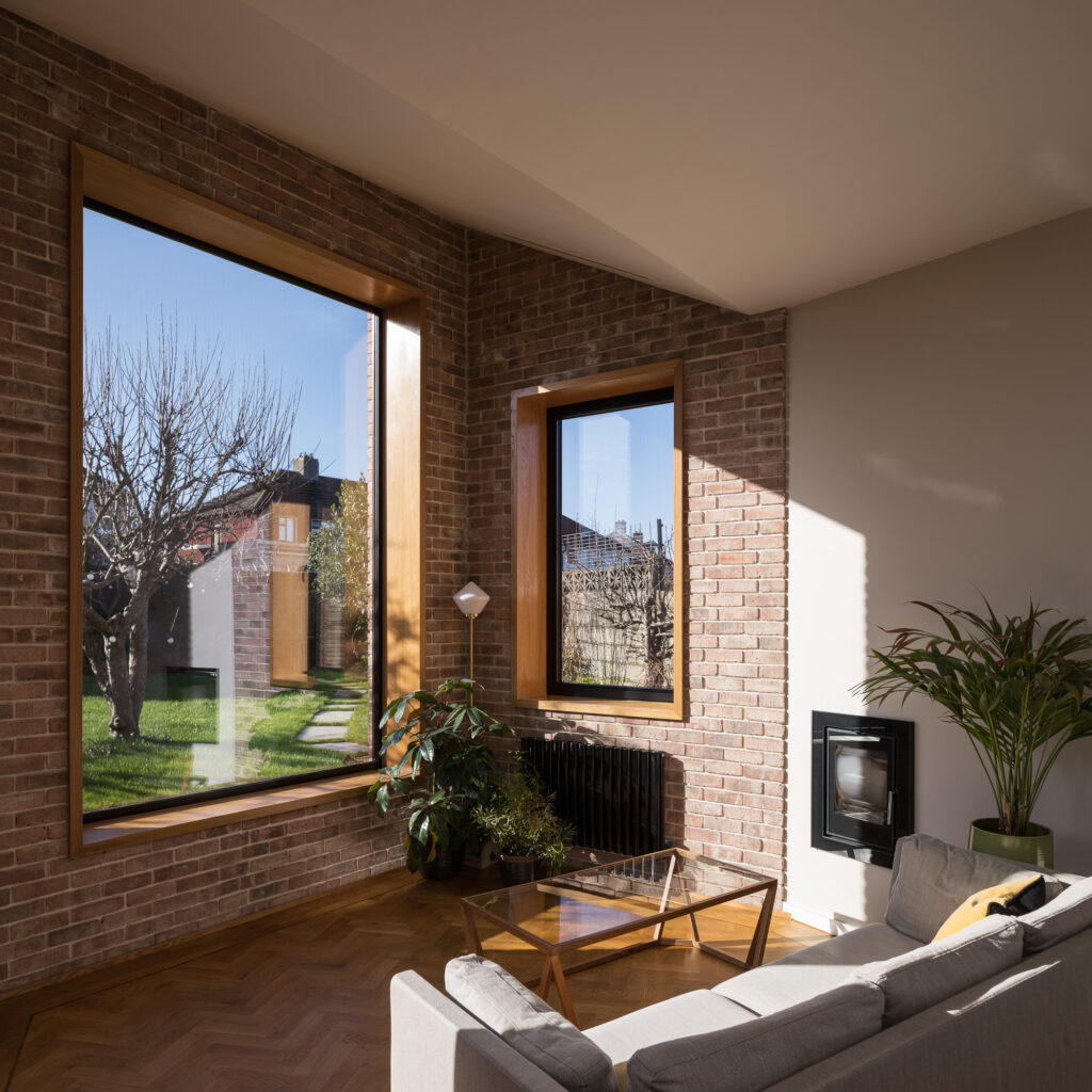 living-area-with-angled-roof-and-brick-and-white-plastered-wall-with-view-to-garden-through-timber-framed-windows