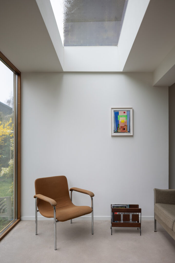 white-walled-living-area-with-exposed-concrete-floors-and-flat-roof-window-over-brown-arm-chair