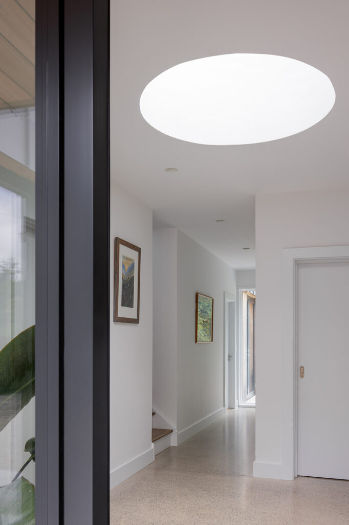 white-walled-hallway-with-frame-of-black-door-with-circular-roof-light-in-the-ceiling