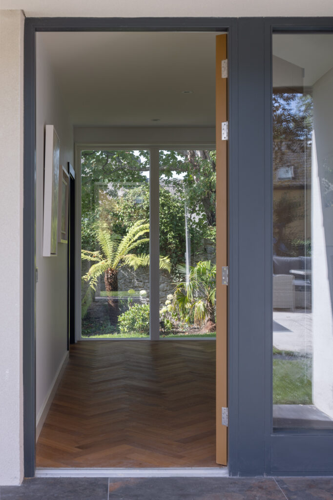 open-door-to-herringbone-timber-floor-with-with-view-towards-glazed-opening-to-garden