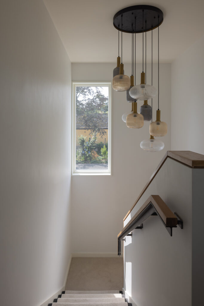 carpeted-stairway-with-wooden-handle-and-wooden-topped-balustrade-with-hanging-glass-lights-and-window-to-garden